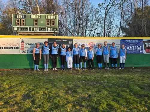 A baseball team in light blue jerseys lined up in front of a scoreboard.