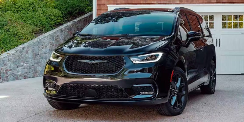 A black Chrysler Pacifica minivan parked on a paved driveway in front of a house.