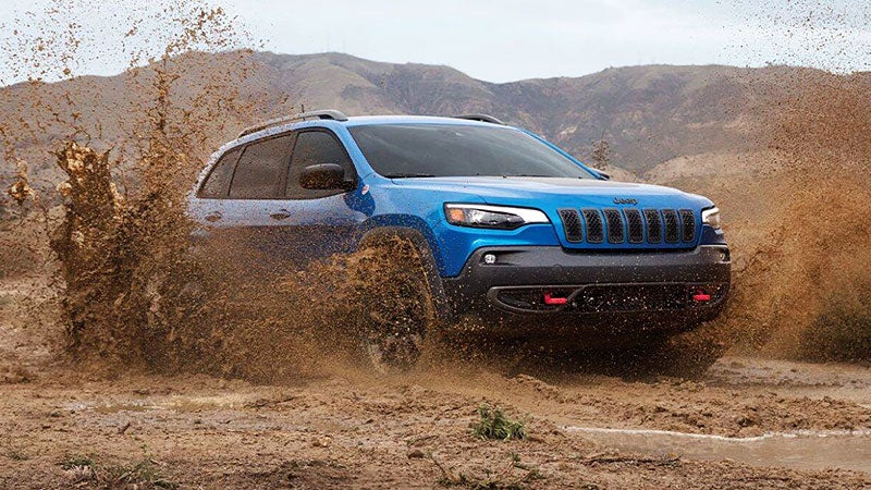Jeep Cherokee driving fast through a muddy puddle, splashing mud on all sides.