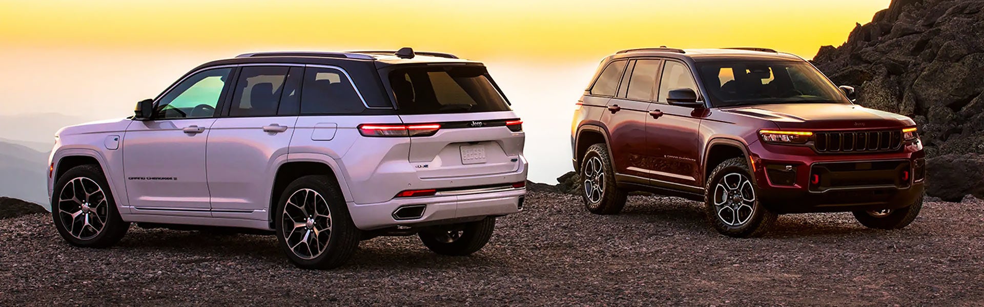 Two Jeep Grand Cherokee SUVs on a rocky terrain against a sunset sky.
