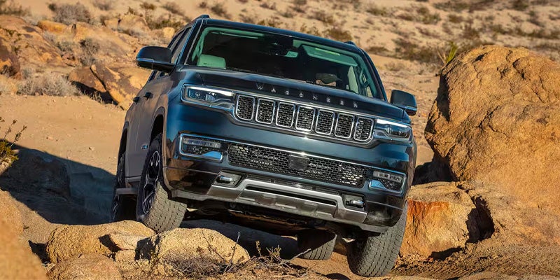 Front view of a dark blue Jeep Wagoneer on a rocky off-road trail in a desert landscape.