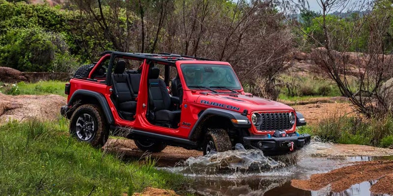 Red Jeep Rubicon 4-door off-roading through water in nature