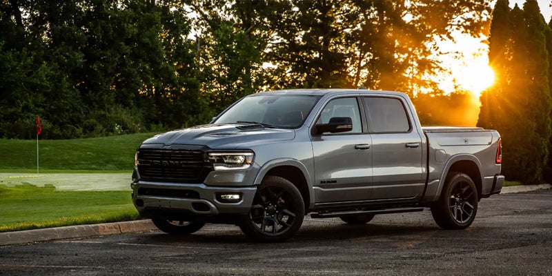 A gray pickup truck with black wheels parked near a golf course at sunset.
