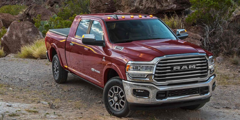 A shining cherry-red Dodge Ram truck is parked on a dirt path in a desert landscape.