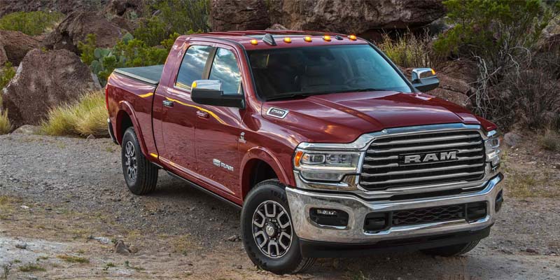 A maroon Ram 2500 pickup truck with a chrome grille on an unpaved road in a rocky, arid landscape.