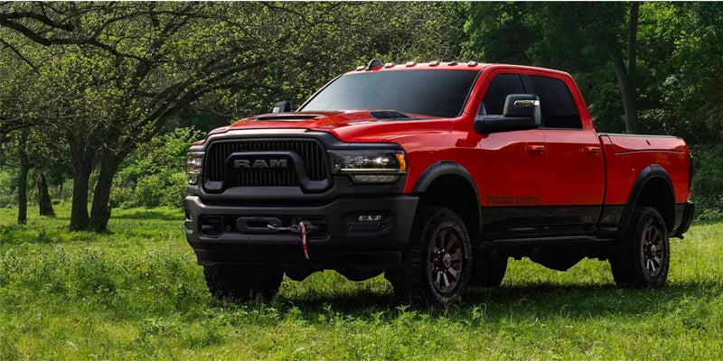 A red Ram Power Wagon pickup truck is parked in a grassy field with trees in the background.