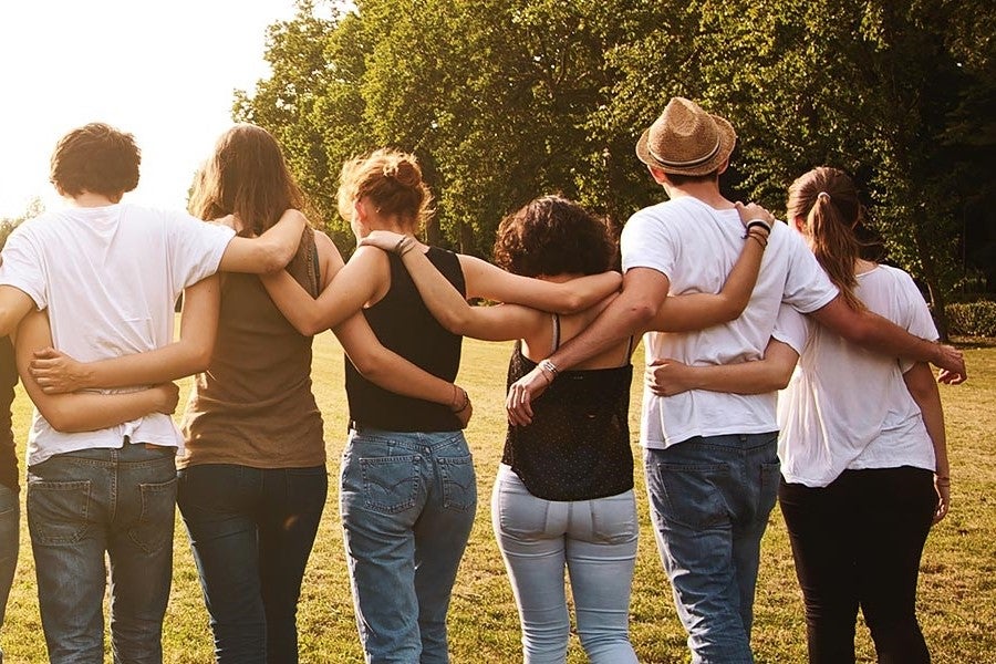 Six friends standing in a line with arms around each other's shoulders